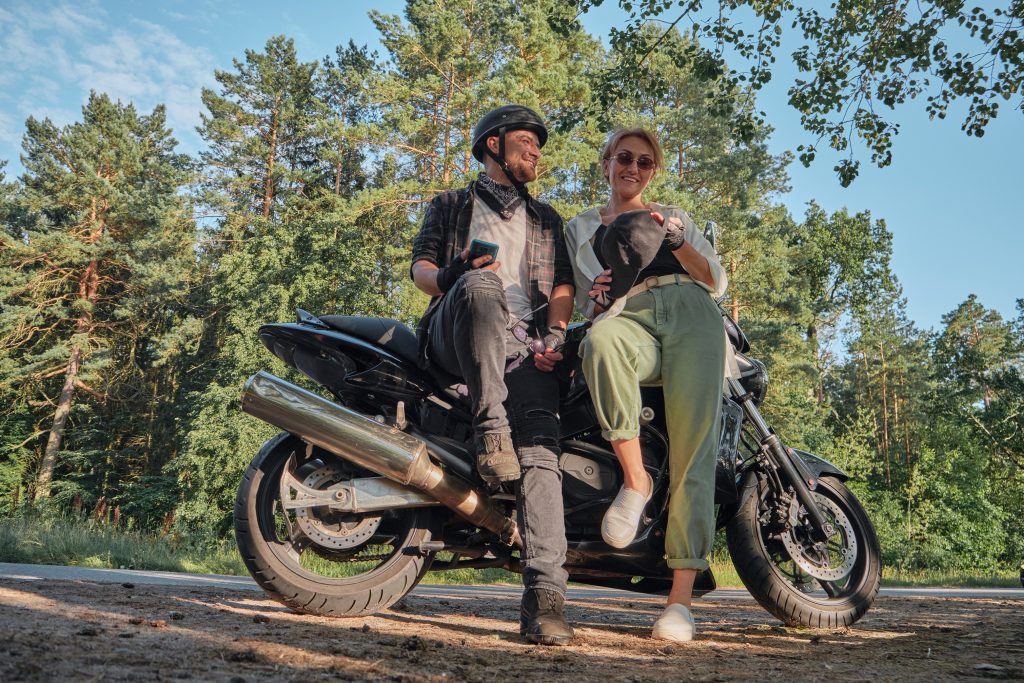 Middle age couple talking and having fun, sitting on a motorcycle, traveling together on a forest road.