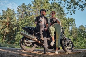 Middle age couple talking and having fun, sitting on a motorcycle, traveling together on a forest road.